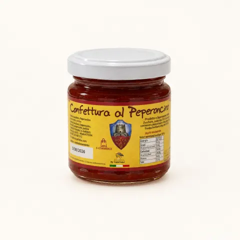 Glass jar filled with red chilli jam, yellow label with product details, white lid.